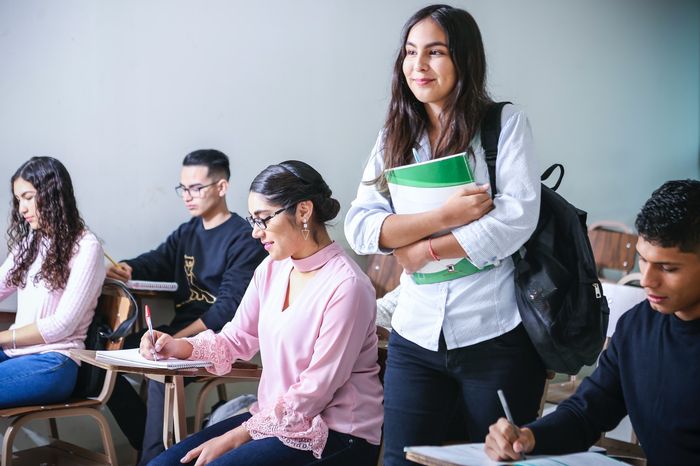 A university student stood up in a lecture holding books.